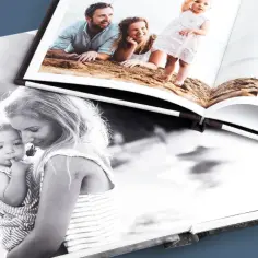 Otwarta fotoksiążka z rodzinnymi zdjęciami na plaży. Na jednej stronie czarno-białe zdjęcie mamy z dzieckiem, na drugiej kolorowe ujęcia rodziny.