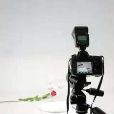 Profesjonalna fotografia produktowa: aparat na statywie, błyskawica, talerze, kieliszki i róża tworzą romantyczną scenę.