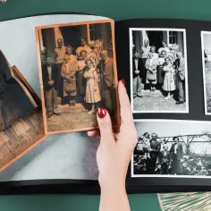 Dłonie układają stare fotografie w albumie, rozpoczynając proces digitalizacji zdjęć. Widać rodzinne portrety i dzieci.