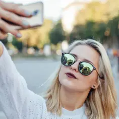 Dziewczyna robi sobie selfie w okularach przeciwsłonecznych, w tle miejski plac.