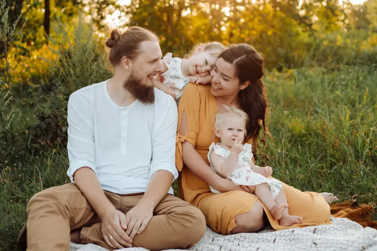 Urocza rodzina podczas sesji zdjęciowej dzieci pomysły. Mama, tata i dwie córeczki siedzą na kocu w trawie, otoczeni złotym światłem.