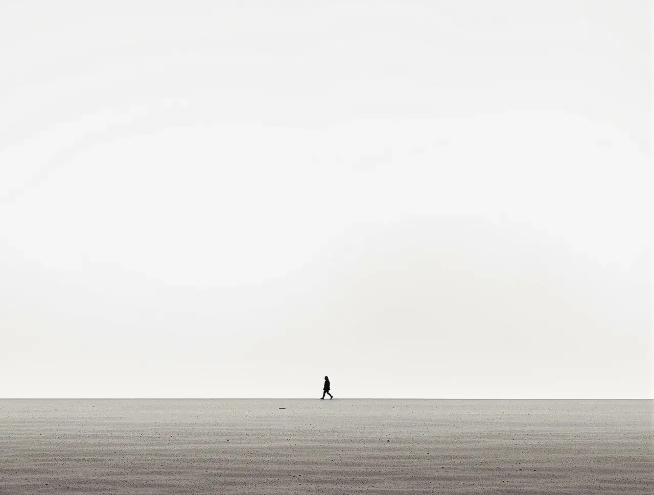 Samotna postać na pustej plaży, idealny przykład minimalizmu w fotografii.