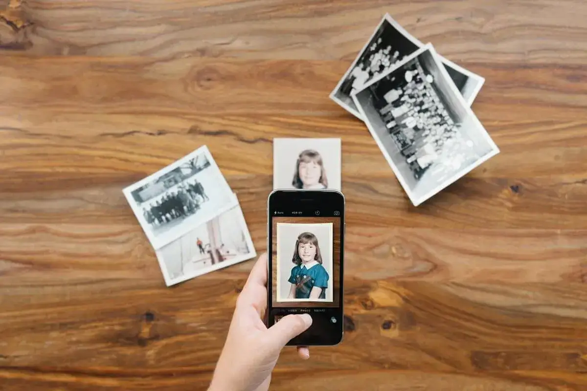 Skan ze zdjęcia: dłoń trzyma smartfon, na którym widać zdjęcie dziewczynki. Obok leżą stare fotografie.